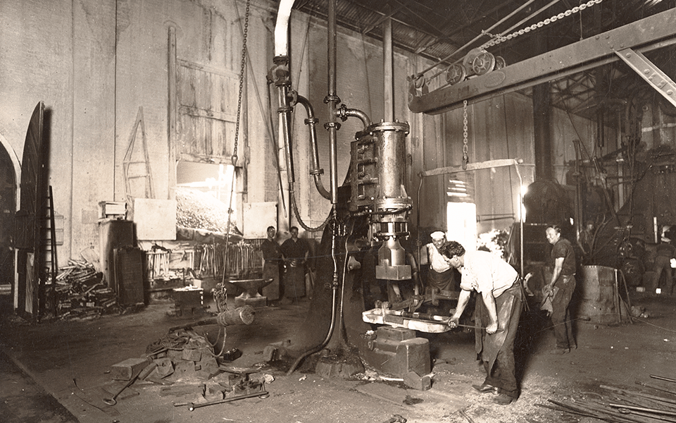 Blacksmith forging a locomotive foundation bar on a steam hammer in the Blacksmith Shop.
